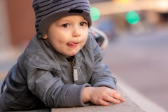 Toddle boy wearing a grey jacket and hat making a funny face with bokeh in the background