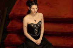 Woman in black prom dress sitting formally on red velvet stairs