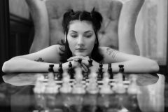Black and white image of woman thinking while looking at a chess set