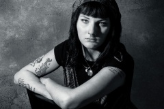 Black and white image of a woman with tattoos sitting on a chair making a somber look