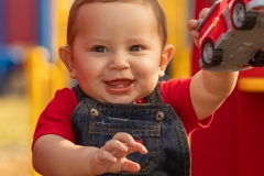 Infant boy in red shirt and denim overalls with a red toy firetruck